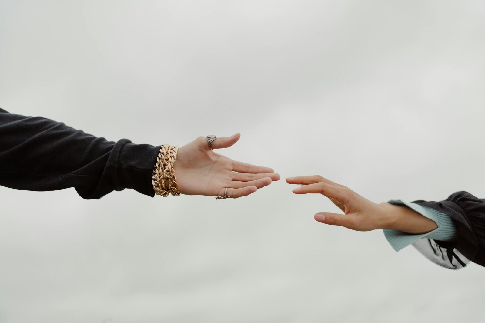 Close-up of two hands reaching for each other under a cloudy sky, symbolizing connection.